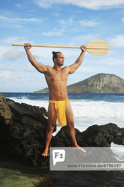 Hawaii  Oahu  Makapuu  polynesische Mann in traditionelle hawaiische auf felsiges Ufer ein Paddel hält Kleidung.