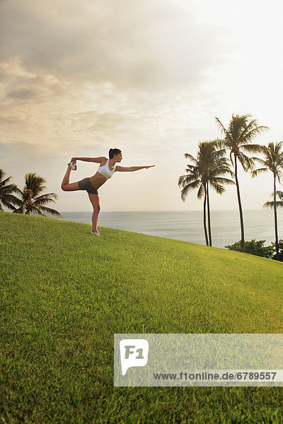 Hawaii  Oahu  weiblich tun eine Yoga darstellen  auf einem Hügel mit Blick auf Meer  Palmen und den Sonnenuntergang.