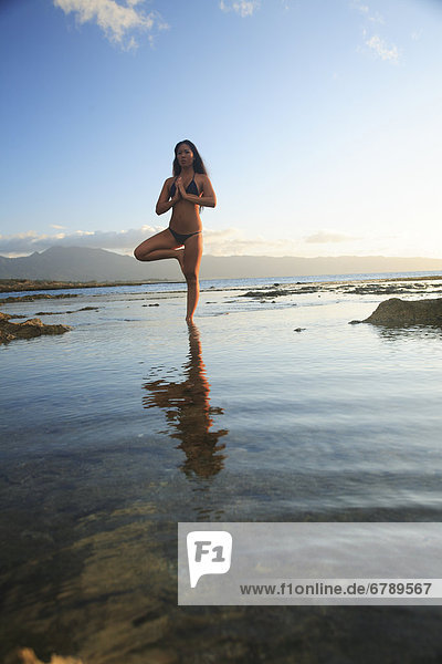 Hawaii  Oahu  Fit young girl on the beach doing yoga on the rocky coastline.