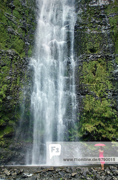 Hawaii  Maui  Kipahulu  Hana  Frau steht mit Sonnenschirm am Fuße des Wasserfalls.