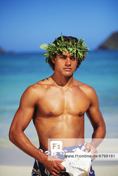 Young Polynesian man with haku on beach  holding conch shell in hands
