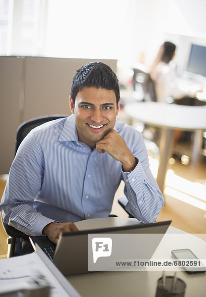 Businessman working on laptop  businesswoman in background