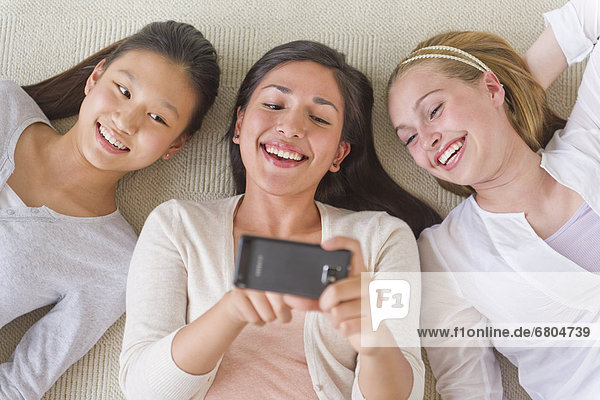 Friends (14-19) lying on floor looking at mobile phone