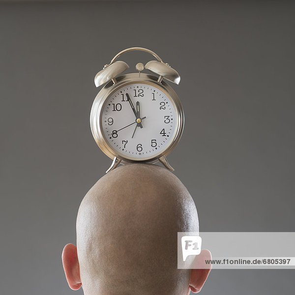 Back view of man with alarm clock on shaved head