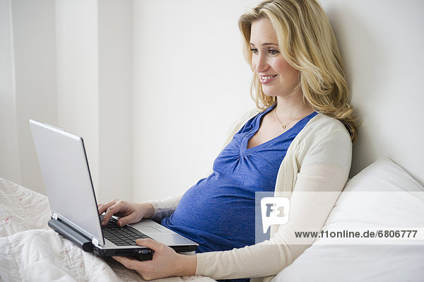 Schwangere Frau benutzt einen Laptop im Bett