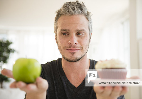 Man weighing green apple against cup cake