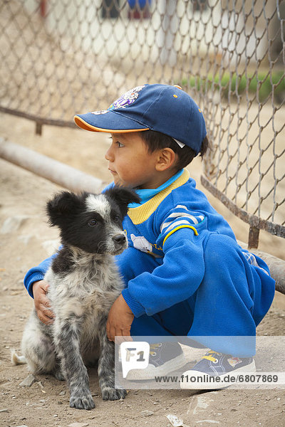 A young boy crouches down to touch a dog  lima peru