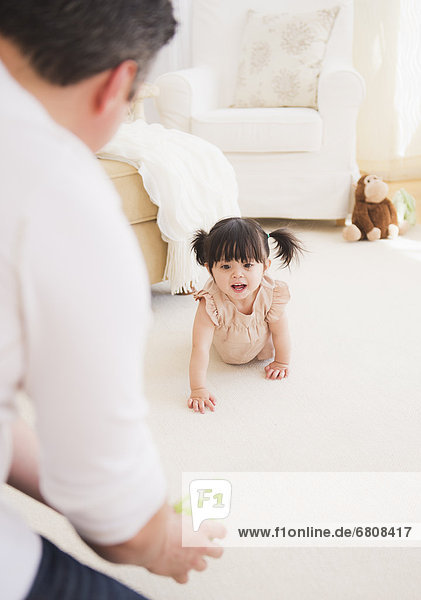 Father encouraging baby daughter (12-17 months) to crawl