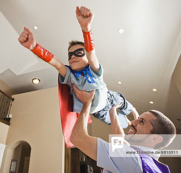 Father holding aloft his son (8-9) dressed up in fancy dress costume