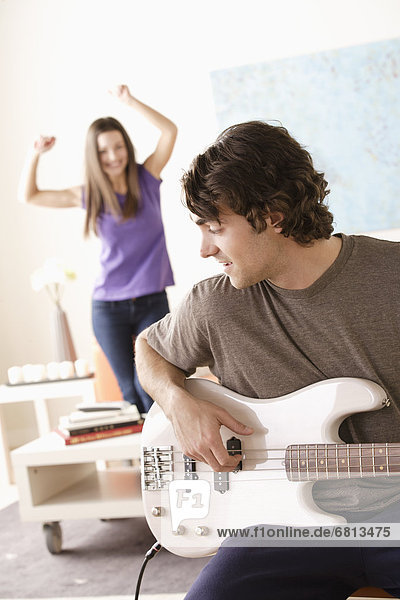 Young man playing electric guitar young woman dancing in background