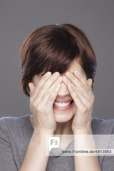 Studio shot of young smiling woman covering face with hands