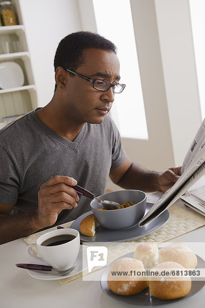 Mature man eating breakfast and reading newspaper