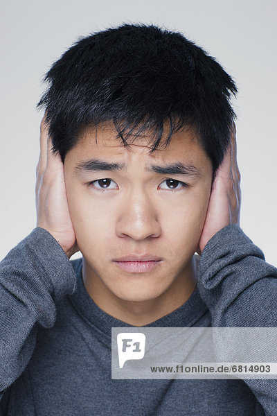 Studio portrait of young man covering ears