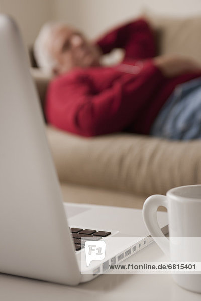 Senior man sleeping on sofa  laptop and mug in foreground