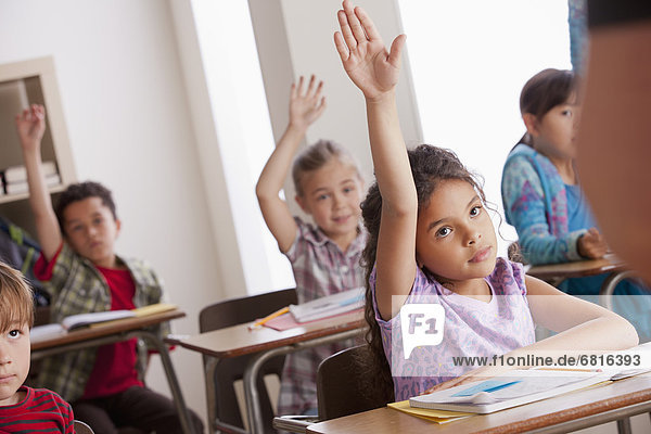 Pupils in classroom raising hands
