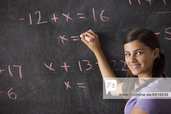 Portrait of schoolgirl (12-13) standing in front of blackboard during math classes