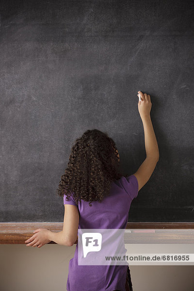 Portrait of schoolgirl (10-11) writing on blackboard
