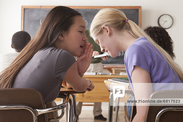 Teenage girls (14-15 16-17) whispering in classroom