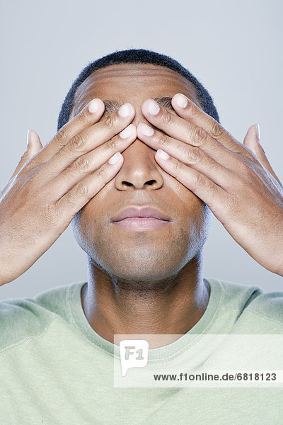 Young man with hands covering eyes  studio shot