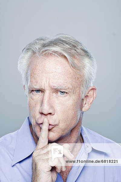 Portrait of senior man with finger on lips  studio shot