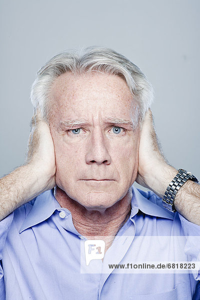 Portrait of senior man covering his ears  studio shot