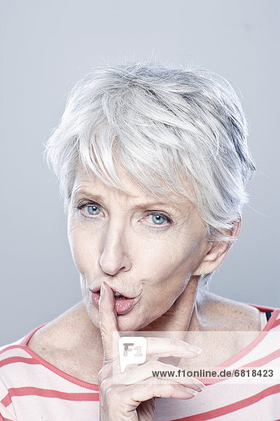 Portrait of senior woman with finger on her lips  studio shot