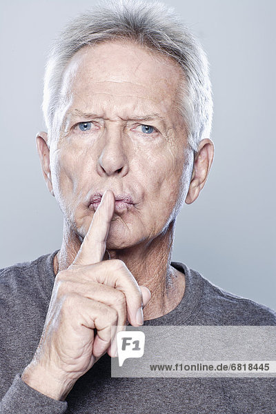 Portrait of senior man with finger on his lips  studio shot