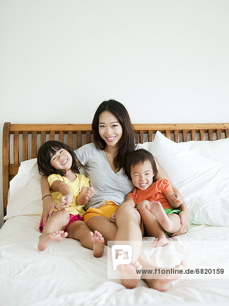 Portrait of mother with daughters (2-3  4-5) sitting on bed