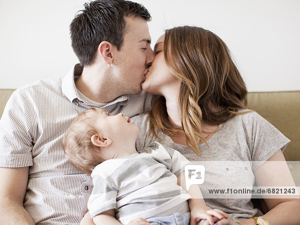 Young couple kissing with baby boy (6-11 months) on their lap