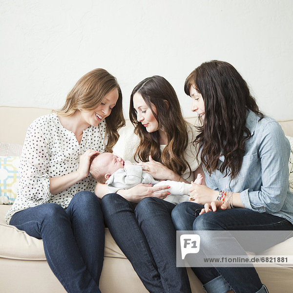 Three young female friends sitting on sofa with baby boy (2-5 months) o0n their lap