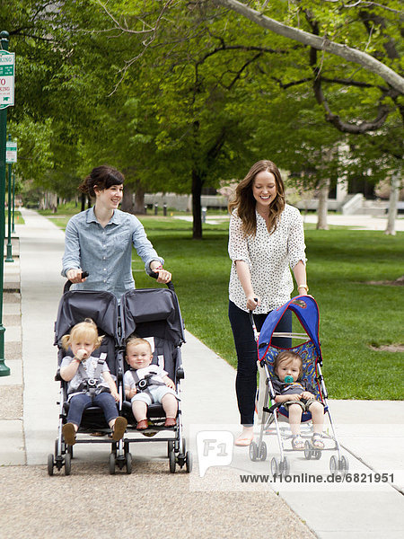 USA  Utah  Salt Lake City  Two young mothers walking with two baby boys (6-11 months) and toddler girl (2-3) in push prams