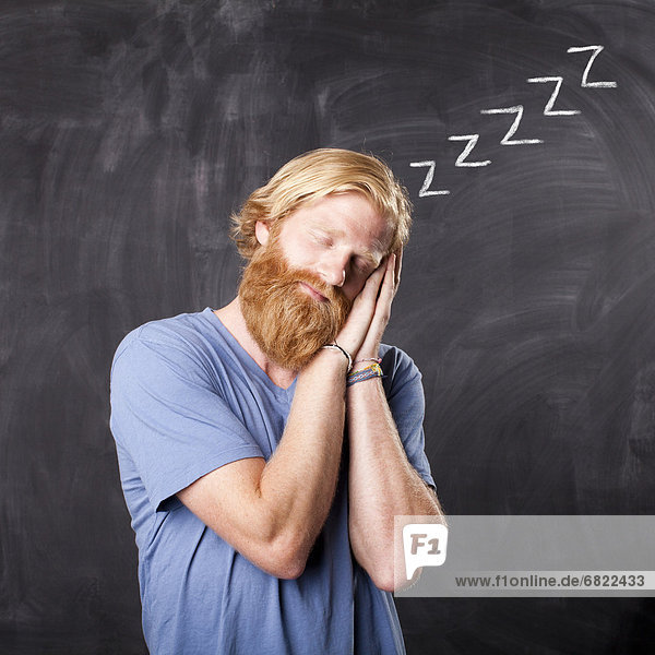 Man sleeping while standing in front of blackboard