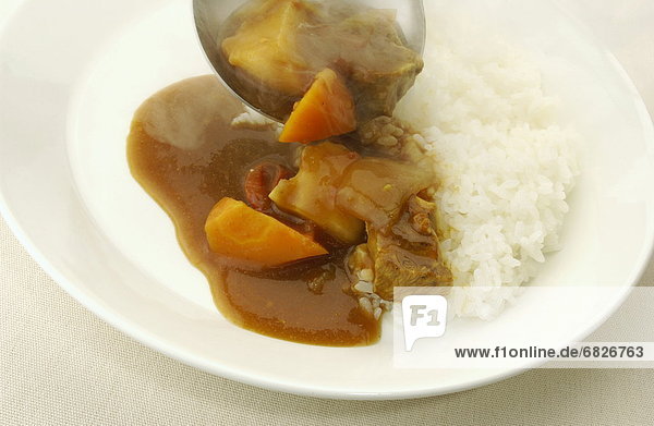 Curry being poured on plate of rice  white background