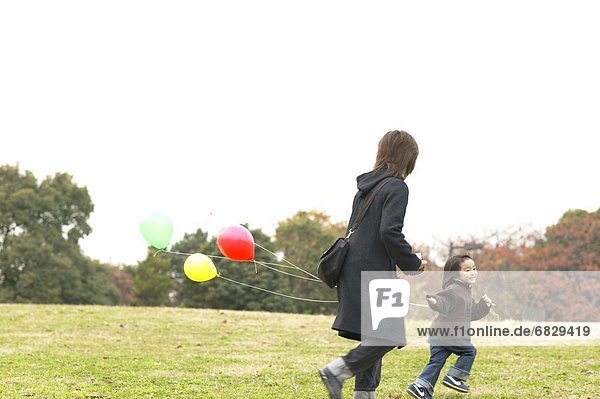 Mother and young daughter running with balloons in a park