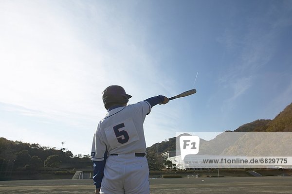 Boy in baseball uniform standing in field  holding up baseball bat