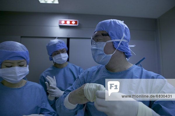 Three surgeons in surgical wear  taking off gloves