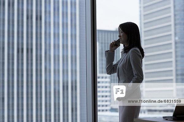 Businesswoman standing by window and on cell phone