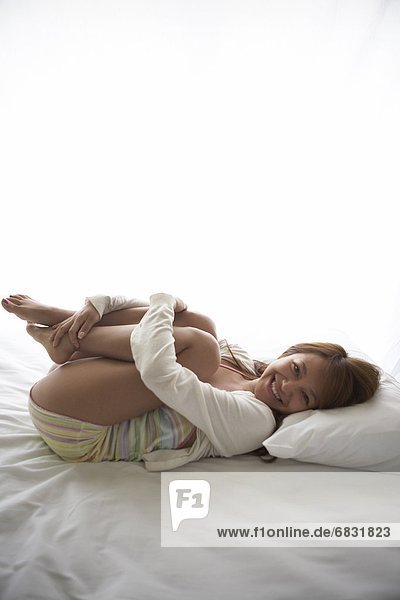 Young woman hugging knees on bed