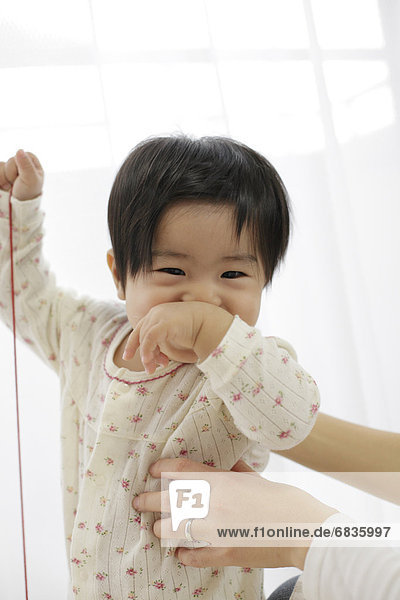 Baby holding string and covering mouth with hand