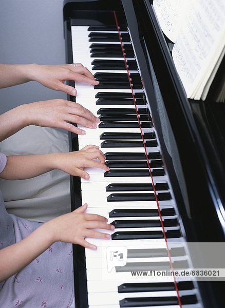 Hands of a mother and daughter playing a piano