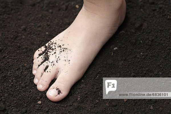 A child's foot covered in dirt on the ground
