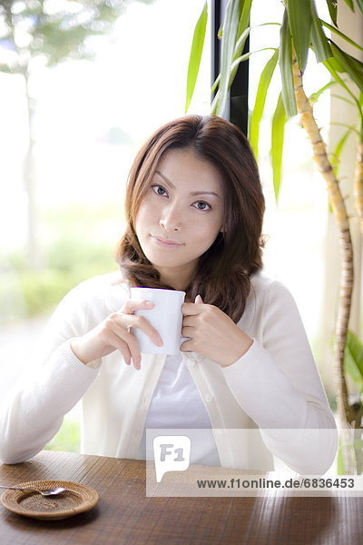 Portrait of young woman holding mug in cafe  smiling and looking at camera