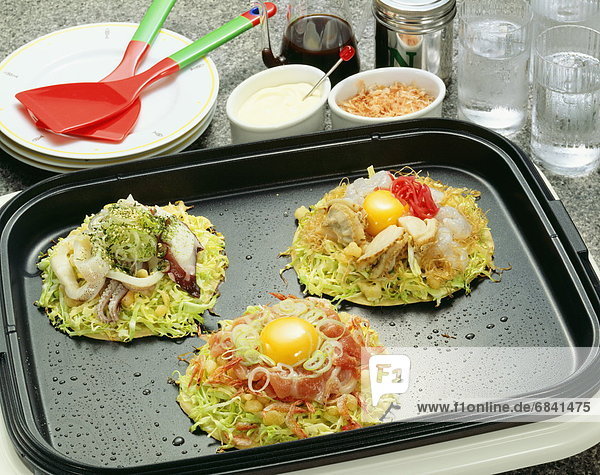 Japanese pancakes containing variety of ingredients on hot plate