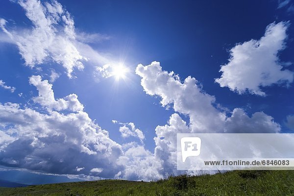 Sun shining in a cloudy blue sky over grasslands. Nagano Prefecture  Japan