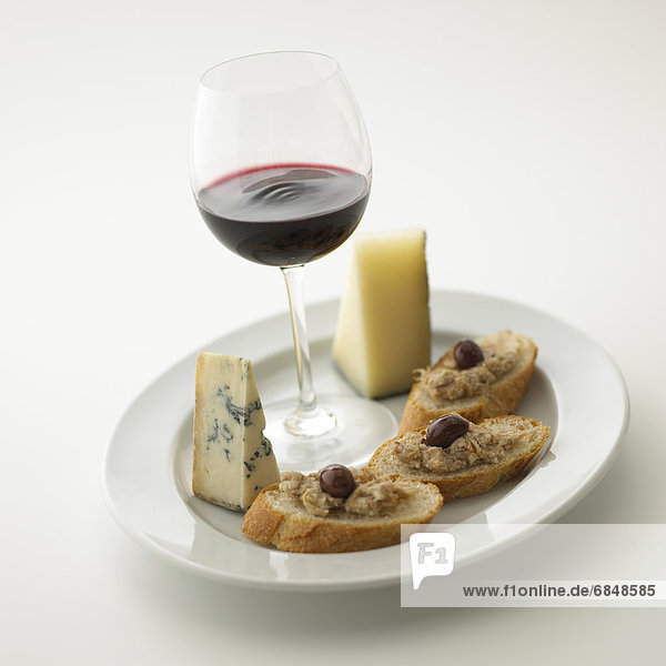 Glass of red wine and plate of cheese and bread  white background