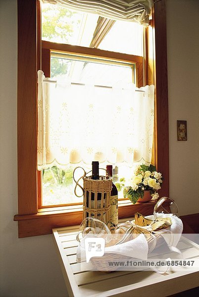 Two Bottles of Wine and a Gift Basket With Wine Glasses on a Window Sill