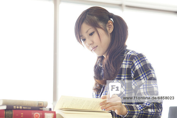 Young woman reading a book in a library  Japan