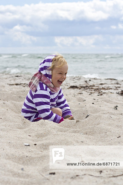 Fröhliches Mädchen spielt im Sand am Strand