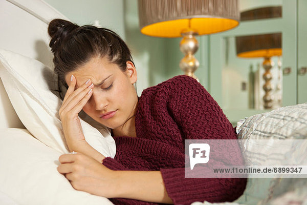 Junge Frau im Bett mit Kopfschmerzen