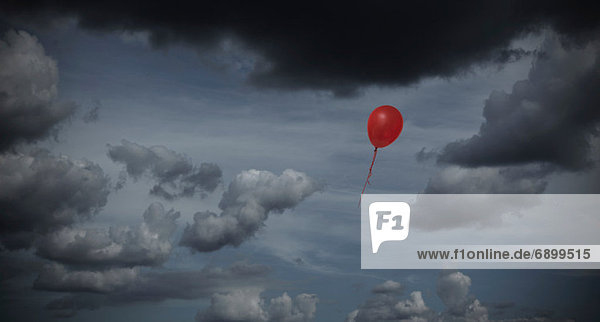 Red balloon floating through dark sky